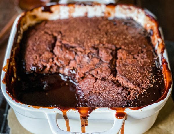 Close up of the Chocolate Self Saucing Pudding in a square, white ovenproof dish with gooey chocolate sauce visible in the bottom of the dish.