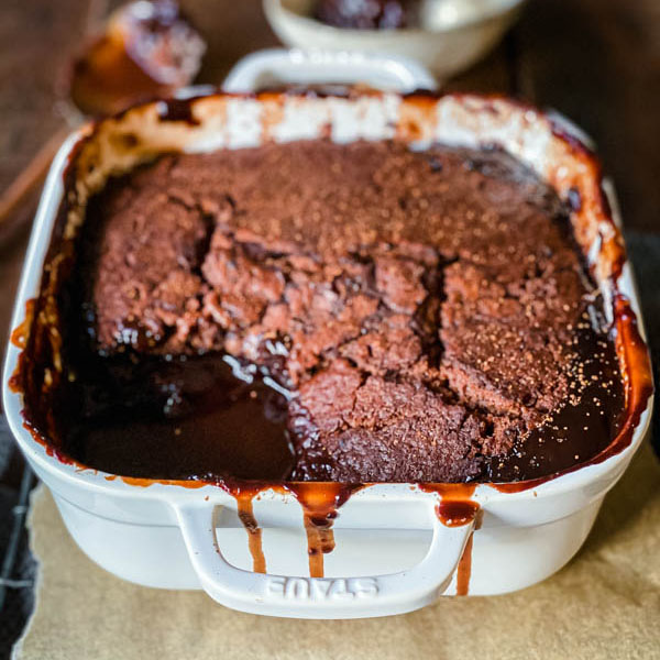 Close up of the Chocolate Self Saucing Pudding in a square, white ovenproof dish with gooey chocolate sauce visible in the bottom of the dish.