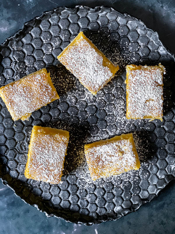 Looking down onto the black textured honeycomb patterned plate with the 5 slices of Gooey Yuzu Slice that are dusted with icing sugar.