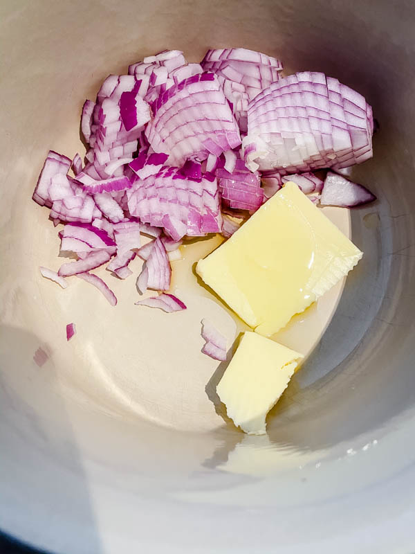 Looking into a pot that has a chopped red onion, butter and oil in it.