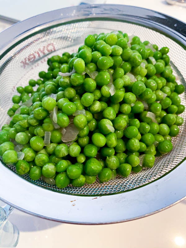 The green baby peas and onions have been strained into a strainer, ready to be blended.