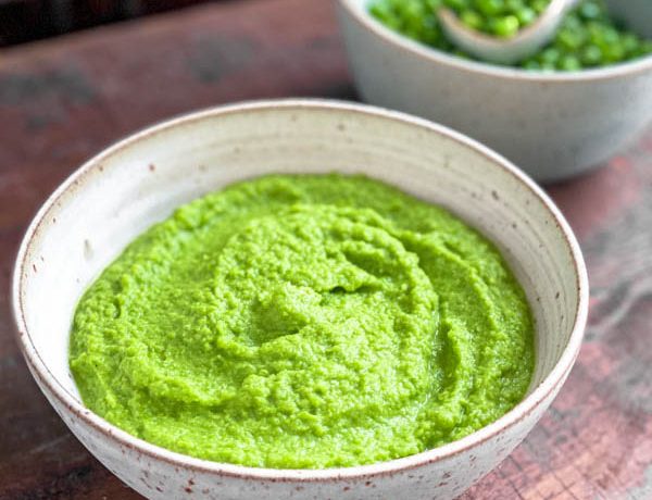 Close up of the bowl of vibrant green Pea Purée with a second bowl of whole peas behind it.