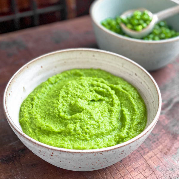 Close up of the bowl of vibrant green Pea Purée with a second bowl of whole peas behind it.
