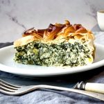 A wedge of Spanakopita Pie served on a white plate with knife and fork in front.