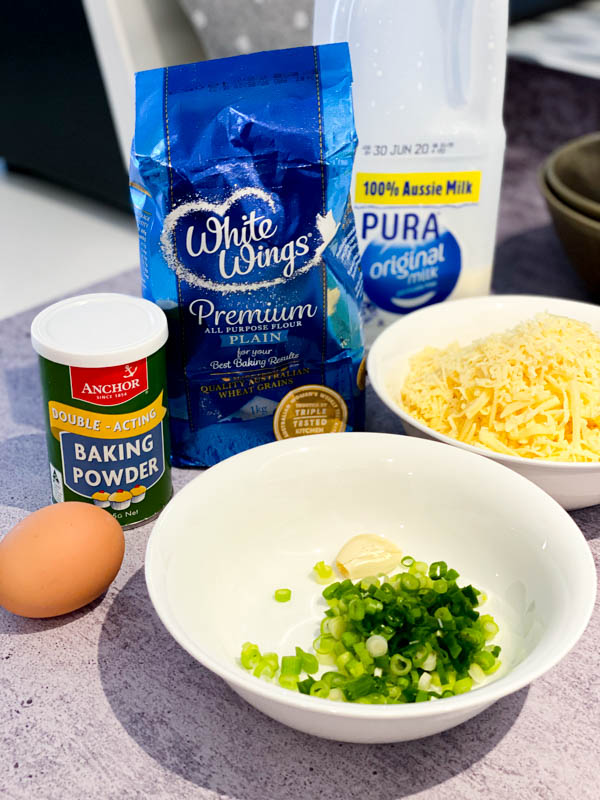 All the ingredients shown to make Cheese Puffs. Flour, milk, cheese, baking powder, spring onions, garlic and an egg.
