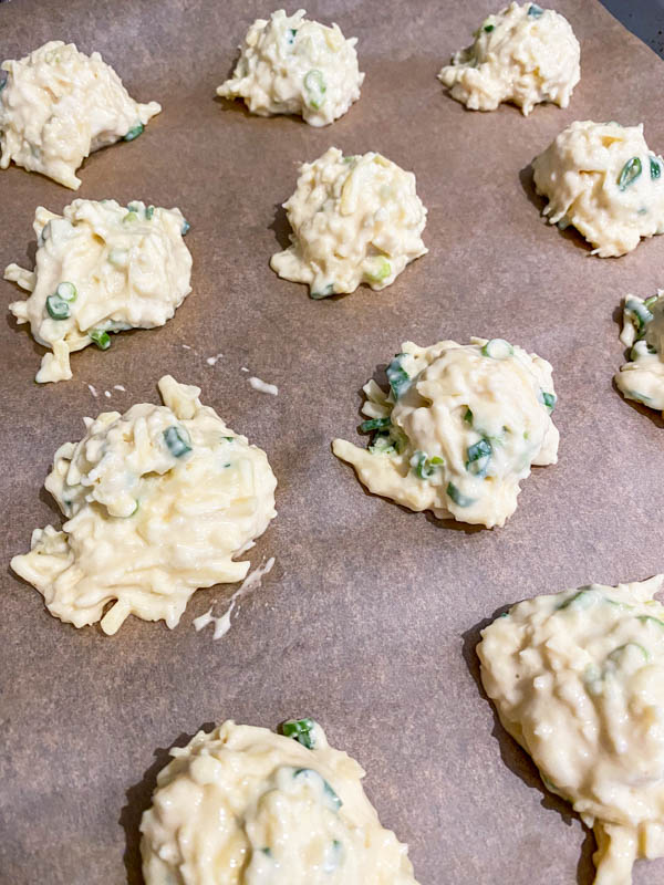 Dollops of Cheese Puff batter are on a baking paper-lined baking tray ready to be baked in the oven.