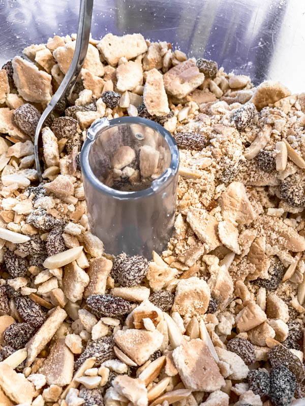 The crushed biscuits, sultanas, nuts and coconut are in the bowl of a food processor.