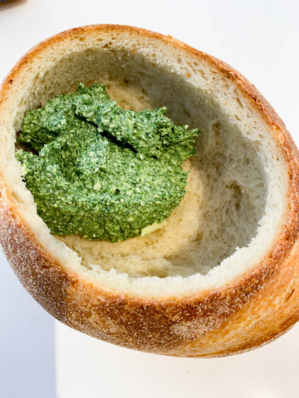 A hollowed out cob loaf with the Spinach Dip mixture being added into the cavity.