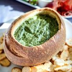 The Spinach Cob Loaf Dip on a white platter with mini bagel crisps around it, ready to be eaten.