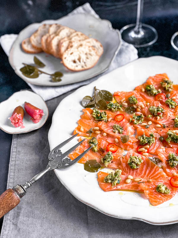 A close up of the Salmon Sashimi platter with a fork leaning up against the side. Next to it is a finger lime cut in half showing the inside pearls and behind that are thinly sliced baguette rounds.