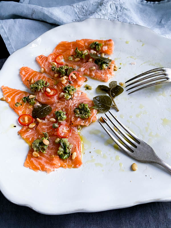 A half empty platter of the salmon sashimi tartare with two forks resting on it. A light grey napkin is draped behind the platter.