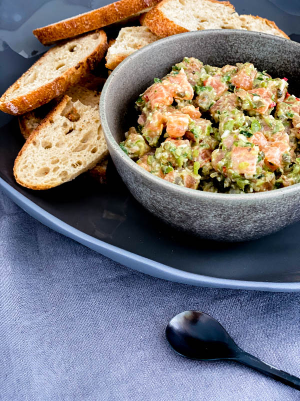 A bowl of Salmon Tartare on a platter with thinly sliced sourdough bread beside it.