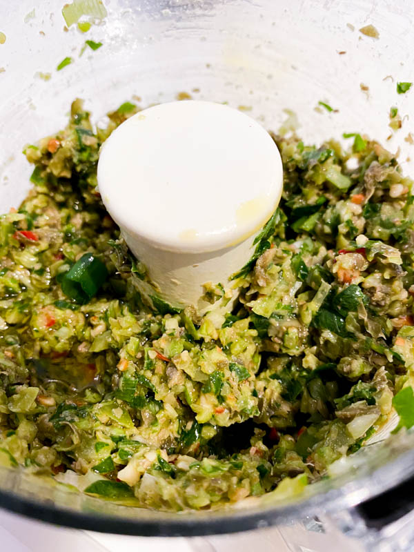 A bowl of a small food processor, showing all the dressing ingredients for the salmon tartare now roughly blitzed together so they still have a chunky texture.
