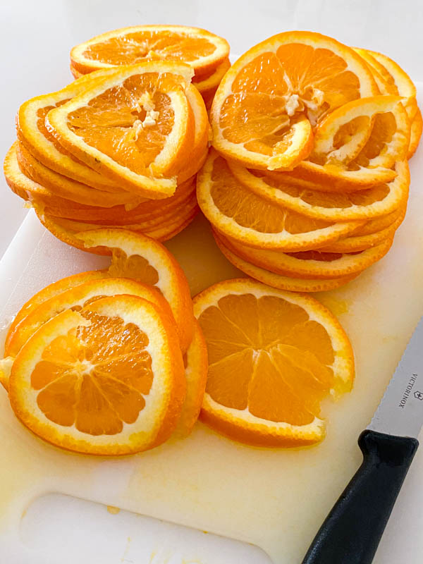 A pile of thin orange slices from 4 oranges sitting on a chopping board.