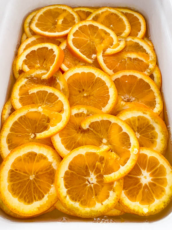 The reduced sugar syrup has now been poured over the orange slices in the large baking dish so they are all covered.