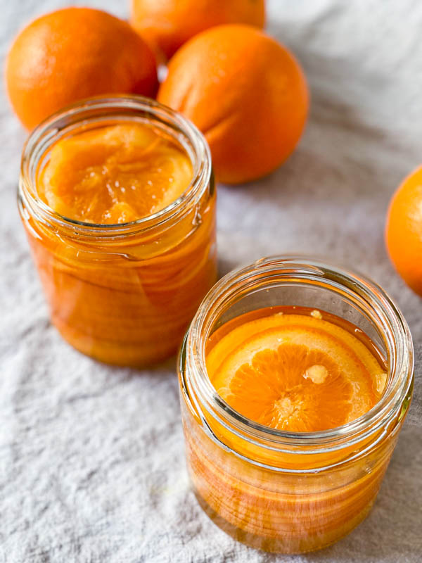 The slices are now cooled an are layered into 2 sterilised jars with the syrup poured in too. In the background are 3 oranges.