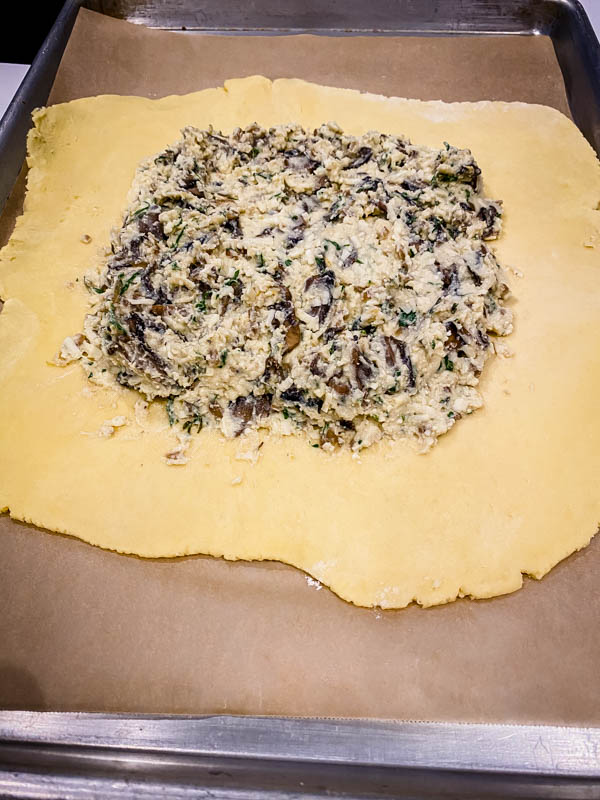 The pastry is rolled out to a 30cm rough circle, with the cheese filling spread out in the middle leaving a 3-4cm border around the outside. The cheese mixture has had 1/2 of the mushrooms mixed into it.