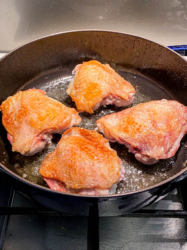 The chicken thighs have been browned on the skin-side and are now turned over to seal the underside.