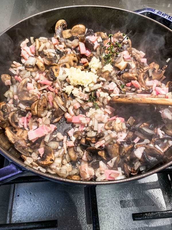 The mushrooms have been browned and now the onions, garlic and bacon have been added to the pan.