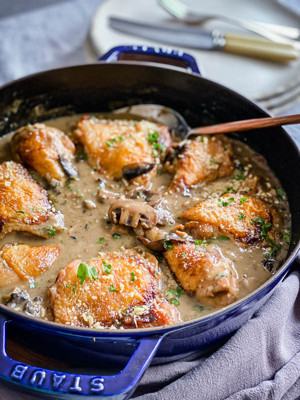 The Chicken, Mushroom and Bacon Bake is in the pan on a table with plates and cutlery behind it.