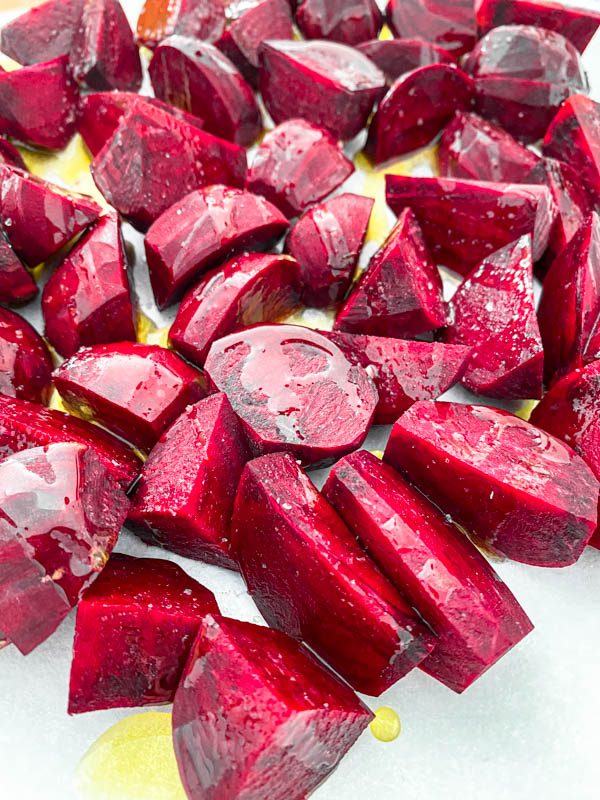 Baby beetroot quarters that have been drizzled with olive oil and seasoned with salt, on an oven tray.