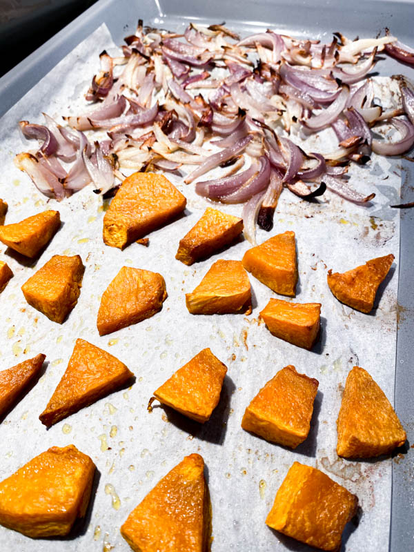 Pumpkin pieces and onion wedges that have been roasted are on an oven tray.