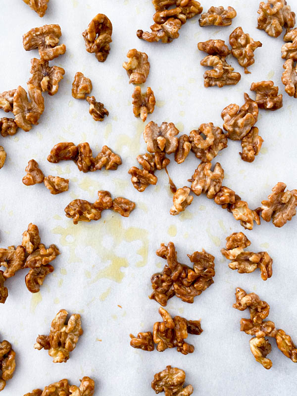 Candied walnut pieces spread out and drying on a piece of parchment paper.