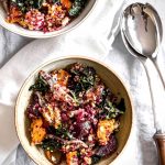 Looking down onto two bowls of salad with a napkin draped between them and wooden handled salad servers to the right.