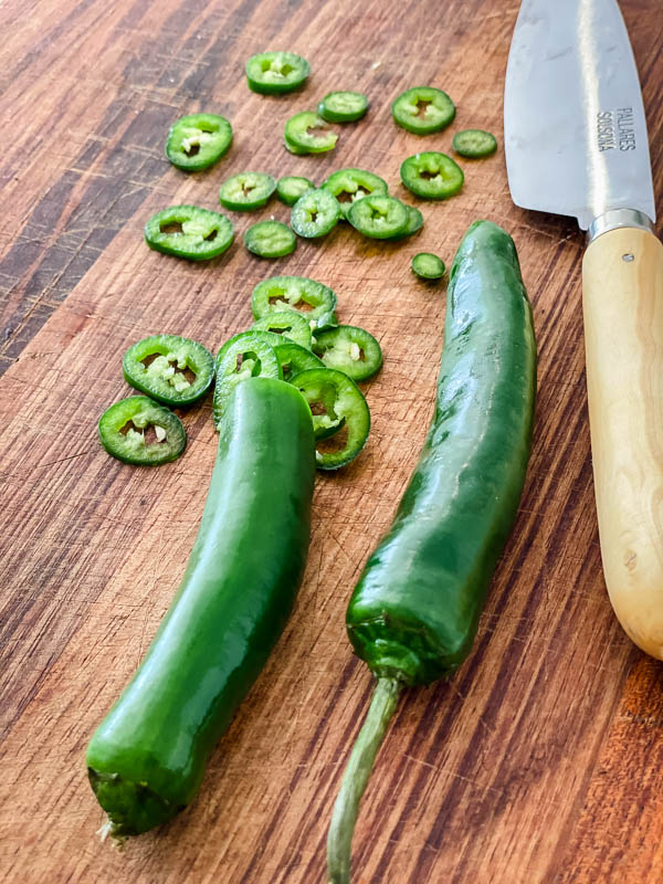 Green Chillies are being sliced on a wooden chopping board.