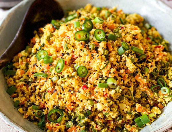 The prepared Cauliflower Fried Rice with Turmeric is in a salad bowl with a serving spoon.
