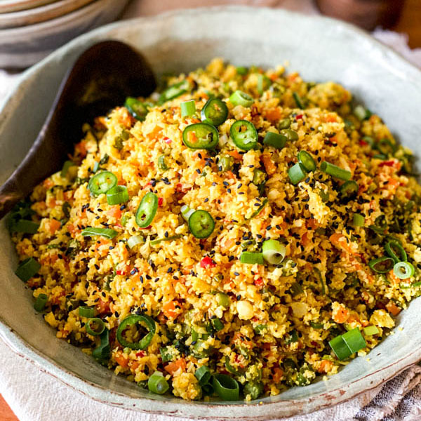 The prepared Cauliflower Fried Rice with Turmeric is in a salad bowl with a serving spoon.