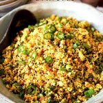 The Cauliflower Fried Rice with Turmeric is in a Salad bowl on a table with bowls in the background and a pinch bowl of sea salt.