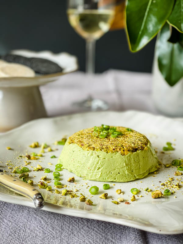 The Avocado Pistachio Pate is on a platter with crackers and a glass of wine in the background.