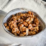 The Candied Walnuts in a bowl on a cream tablecloth.