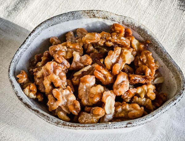 The Candied Walnuts in a bowl on a cream tablecloth.