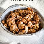 The Candied Walnuts are in a bowl sitting on a cream folded tablecloth.