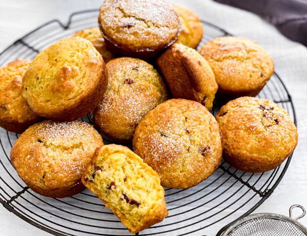 A pile of freshly baked Orange Cranberry Muffins are on top of a vintage cake resting rack.