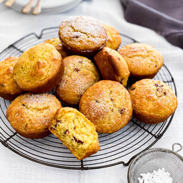 A pile of freshly baked Orange Cranberry Muffins are on top of a vintage cake resting rack.