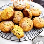 A pile of freshly baked muffins are on a round cake rack. Some are sprinkled with icing sugar.