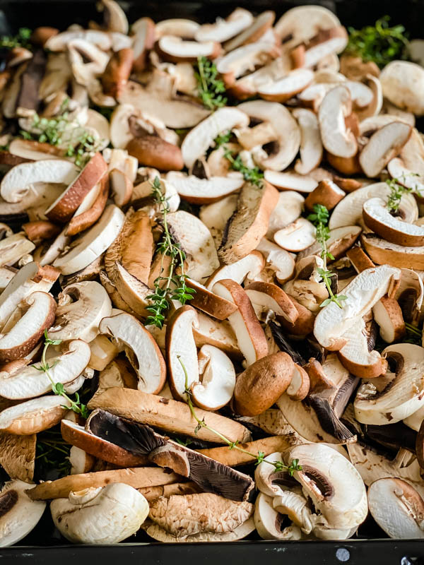 A close up of the raw sliced mushrooms with thyme sprigs scattered over the top.