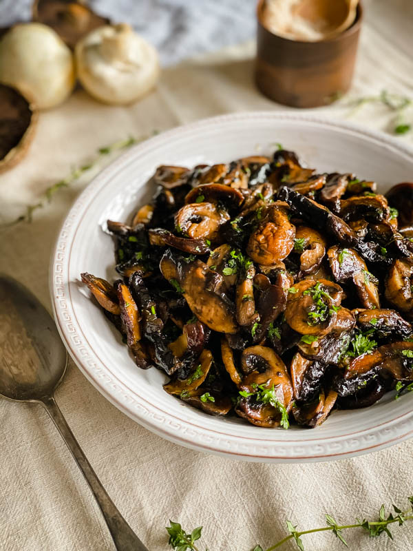 A close up of the bowl of roasted mushrooms with a serving spoon beside it.