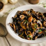 A close up of the Roasted Mushroom Medley in a serving bowl with a serving spoon beside it.