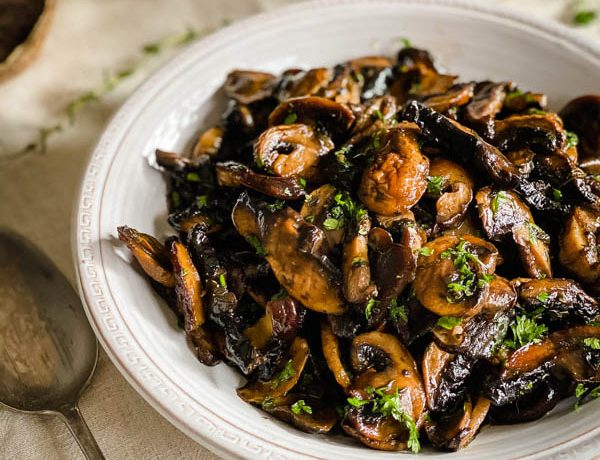 A close up of the Roasted Mushroom Medley in a serving bowl with a serving spoon beside it.