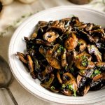 The Roasted Mushroom Medley is in a white bowl on a cream tablecloth.