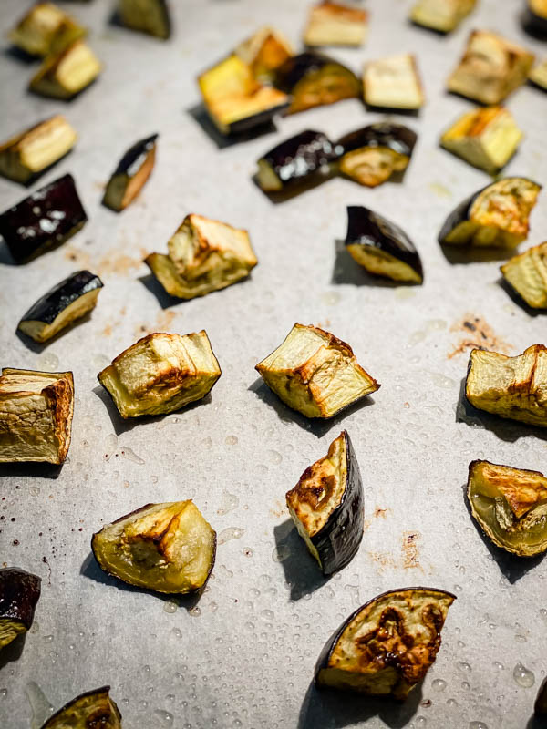 Cubes of roasted eggplant on a baking tray.