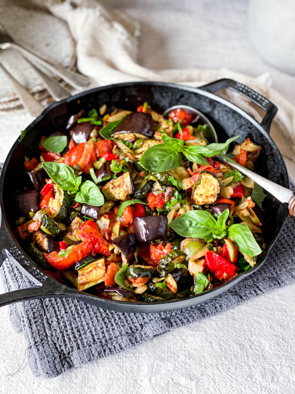 The Roasted Ratatouille Salad is in a black pan on a table with cutlery and plates in the background.