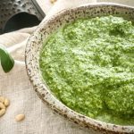 A side close up of the bowl of Basil Pesto which is sitting on top of a linen tablecloth.