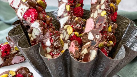 There are 3 long cut slices of rocky road upright in a tin, with some smaller squares of rocky road in front.