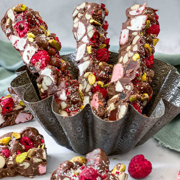 There are 3 long cut slices of rocky road upright in a tin, with some smaller squares of rocky road in front.