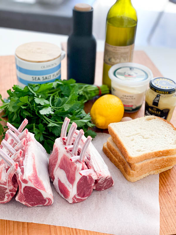 All the ingredients needed to make the Herb Crusted Lamb Racks are all on a large wooden board.